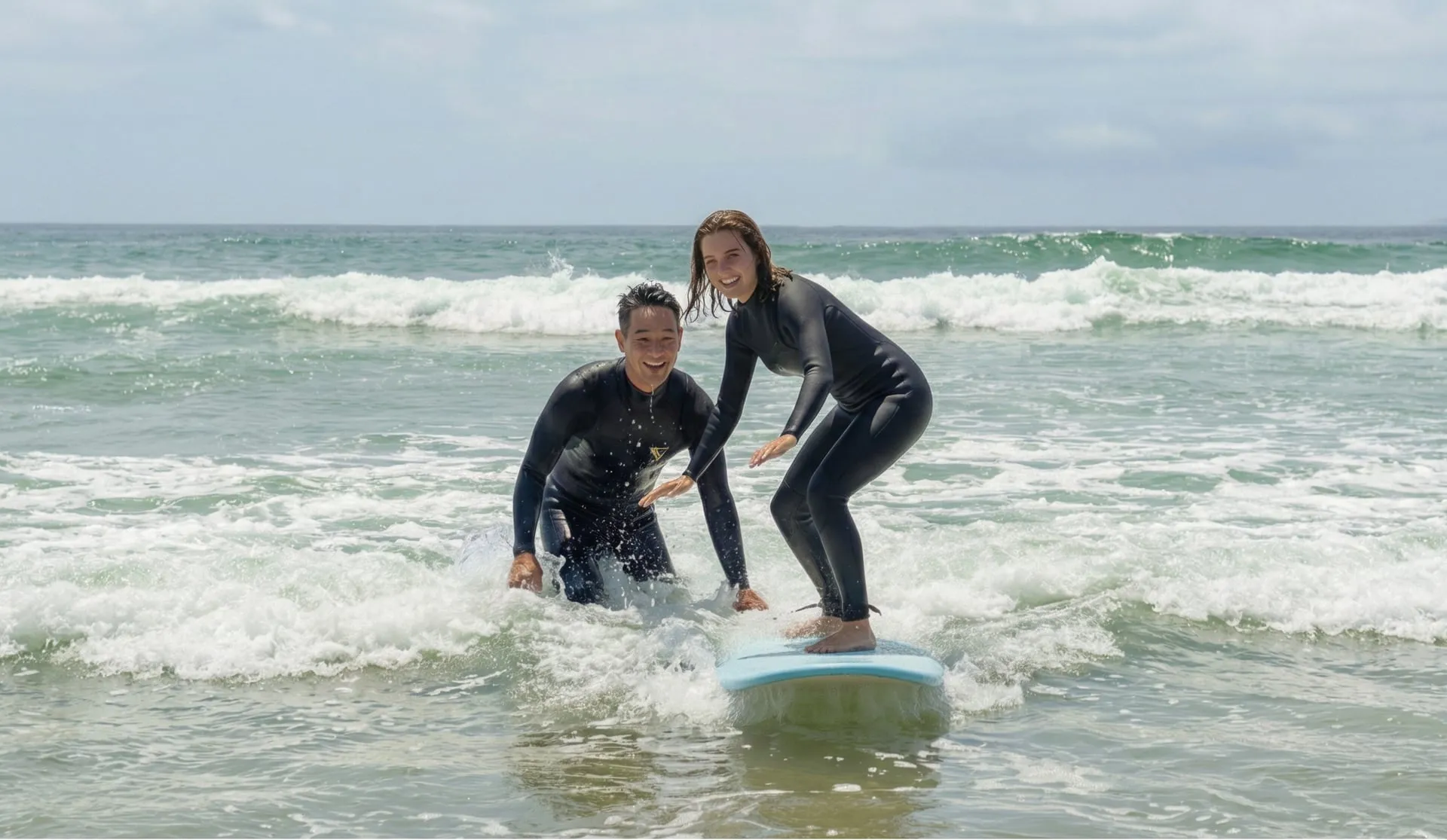 A smiling instructor steadying a beginner as she stands up on a surfboard in the whitewater during a surf lesson near Tokyo.